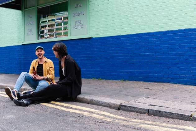 Happy man holding beer bottle sitting with boyfriend on sidewalk model released, Symbolfoto property released, ASGF02863