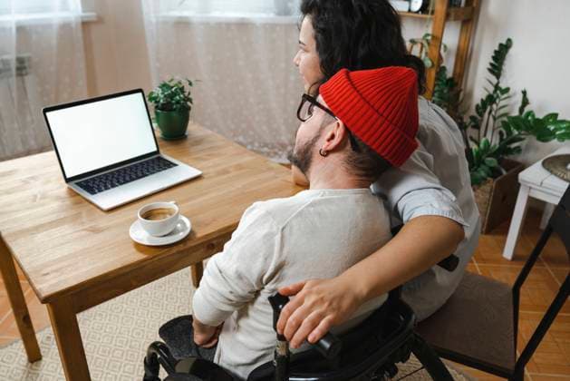 IMAGO Creative, Gesellschaft, Immer mehr Menschen haben Angst vor der Zukunft Woman sitting by boyfriend with disability looking at laptop on table model released, Symbolfoto property released, EKGF00032