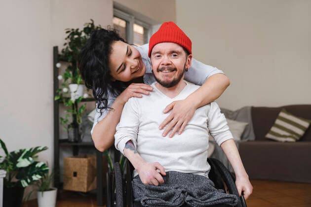 Smiling woman embracing boyfriend in wheelchair at home model released, Symbolfoto property released, EKGF00044