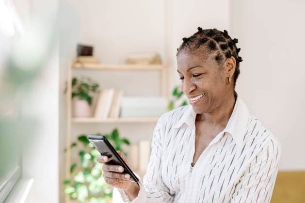 IMAGO Creative: Business, Innovative Technologie-Lösungen Smiling woman using smart phone at home model released, Symbolfoto property released, JCZF01075