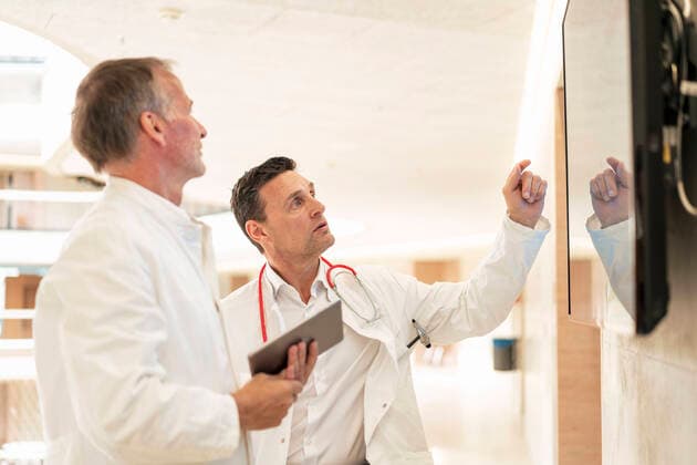 IMAGO Creative: Lokalhelden - Gesundheits- und Rettungskräfte Doctor explaining colleague through screen on wall in hospital model released, Symbolfoto property released, JOSEF12283