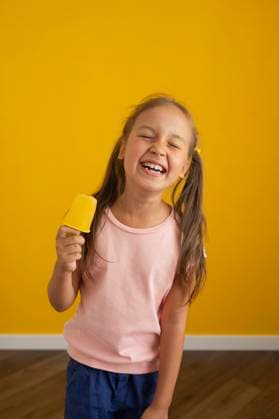 Happy girl standing with ice cream in front of yellow wall model released, Symbolfoto, LESF00158