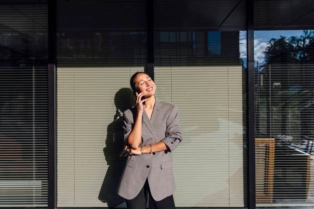 IMAGO Creative: Business, Innovative Technologie-Lösungen Smiling businesswoman with eyes closed talking on mobile phone in front of glass wall model released, Symbolfoto, VPIF07169