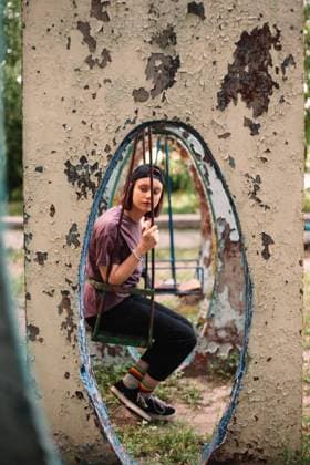Young punk woman sitting on a swing at abandoned playground in summer CR_DMBE220926-1040482-01 ,model released, Symbolfoto
