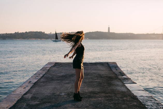 IMAGO Creative, Jahreszeit Sommer, Sommer in der Stadt Attractive charming happy lady in black wear and boots dancing on embankment near water surface with ships in sunny day AlexandraCoelho_PriscillaMarques_12 Copyright: xAlexandraxCoelhox Model Released