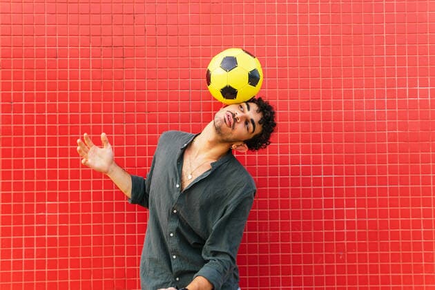IMAGO Creative: 2022 Sport Favoriten Creative Highlights Symbolbilder Young Hispanic man in black shirt balancing yellow football ball on head against tiled red wall on street, Model released DavidMunoz_ID801_29683_019 Copyright: xDavidxMunozx MR