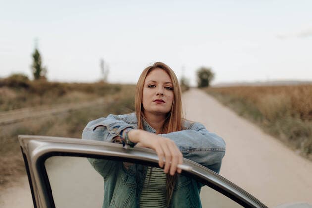IMAGO Creative, Jahreszeit Herbst auf dem Land Confident woman in denim jacket standing with cigarette at car door looking at camera in country ElenaGonzalez_FriendsAutumn_29 Copyright: xElenaxGonzalezx Model Released
