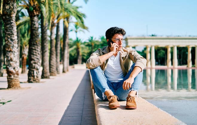 IMAGO Creative, Jahreszeit Sommer, Sommer in der Stadt Stylish pensive male having conversation of mobile phone while sitting near pond in tropical garden in city and looking away, Model released AdalbertoRodriguez_UniversityStudent_16 Copyright: xAdalbertoxRodriguezx MR