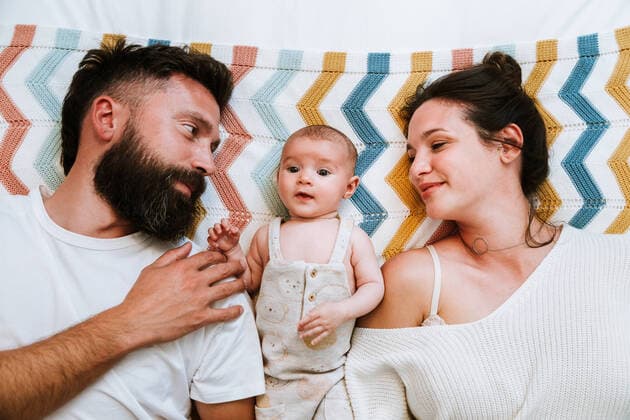Creative Highlights Symbolbilder From above serene baby lying on bed among mother and father cuddling while teasing child, Model released, Property released AntonioOvejero_BabyRed_20 Copyright: xAntonioxOvejerox MR