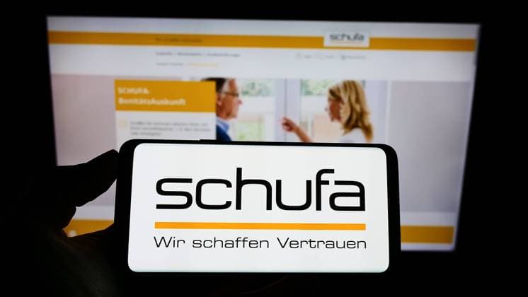 Person holding cellphone with logo of German credit protection company Schufa Holding AG on screen. Stuttgart, Germany - 02-13-2022: Person holding cellphone with logo of German credit protection company Schufa Holding AG on screen in front of web page. Focus on phone display. Copyright: xZoonar.com TimonxSchneiderx zoonar_18996420