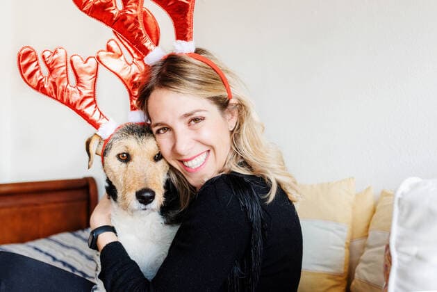 Happy female in decorative deer horns cuddling adorable purebred dog while looking at camera on bed AlbertoMenendez_WomanWithDog_18 Copyright: xx Model Released