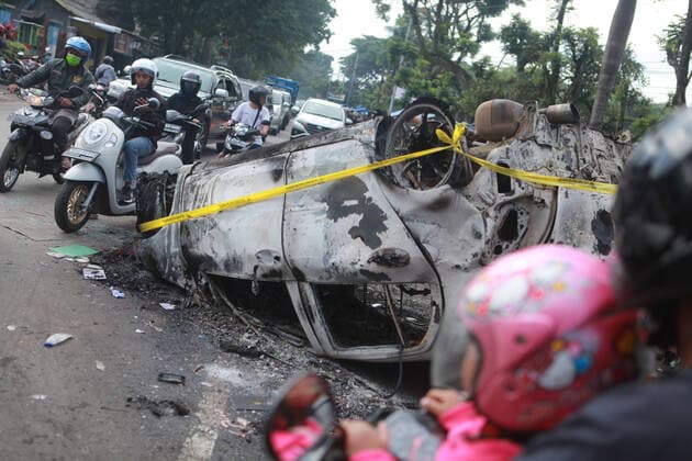 (221002) -- MALANG, Oct. 2, 2022 -- People ride near the wreckage of a burned car outside the Kanjuruhan Stadium in Malang of East Java province, Indonesia, Oct. 2, 2022. At least 129 people were killed and 180 others injured after a stampede and clashes at a football match in Indonesia s Malang, East Java province on Saturday evening, Indonesian police said on Sunday. Provincial police chief Nico Afinta said at a press conference that the chaos happened on late Saturday at the Kanjuruhan Stadium in Malang regency right after Arema Malang club lost to Persebaya Surabaya in the Indonesian Liga 1 football contest. (Photo by Xinhua) INDONESIA-MALANG-FOOTBALL MATCH-STAMPEDE-CLASH-CASUALTIES BayuxNovanta 