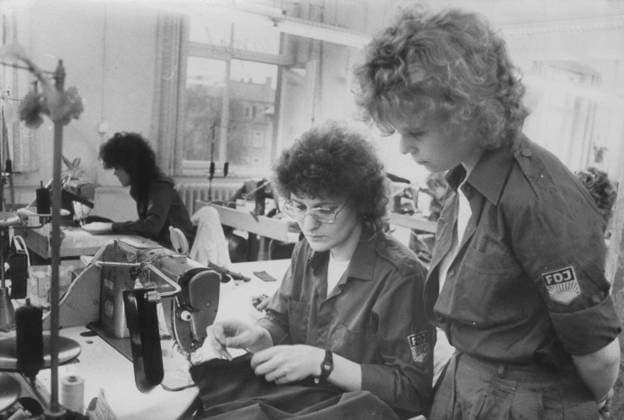 RECORD DATE NOT STATED Sachsen, DDR, Wirtschaft, Betriebe, Arbeit, historisch: Textilindustrie, VEB Herrenmode Dresden, Berufswettbewerb im Kombinat Oberbekleidung; Ines Ender und Iris Fabian (stehend) vom VEB Treffmodelle Berlin in FDJ-Hemd FDJ-Bluse. 15.04.1989. Veröffentlichung in Sächsische Zeitung am 24.04.1989: Mit dem Schiffchen auf den Bermudas ... bewiesen junge Kleidungsfacharbeiter und Facharbeiter für Näherzeugnisse des Kombinates Oberbekleidung Berlin beim Leistungsvergleich in Dresden ihr Geschick Der Wettbewerb zwischen den Besten der 2.300 Jungfacharbeiter findet alle zwei Jahre in einem der 15 Kombinatsbetriebe statt Im VEB Herrenmode ging es kürzlich für die 31 jungen Damen darum, unter den Augen gestrenger Juroren flott und in guter Qu Copyright: xSZ KostasxMargitudisx