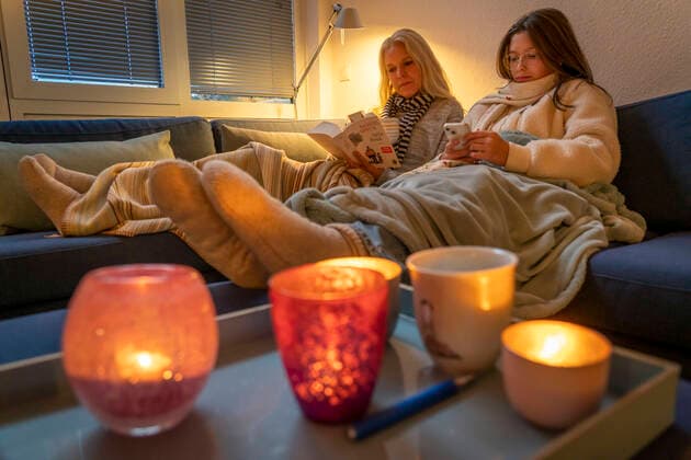 Symbolbild Energiesparen, kalter Winter, Energiekrise, kalte Wohnung, Mutter und Tochter liegen, warm angezogen auf dem Sofa, Kerzenlicht, Heizung auf ein Minimum an, Energiesparen *** Symbol image energy saving, cold winter, energy crisis, cold apartment, mother and daughter lying, dressed warmly on the sofa, candlelight, heating to a minimum on, energy saving.