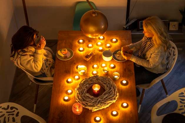 IMAGO Creative: Herbst, Gemütliches Zuhause Symbolbild Energiesparen, kalter Winter, Energiekrise, kalte Wohnung, Mutter und Tochter warm angezogen beim Abendessen, nur bei Kerzenlicht, Heizung auf ein Minimum an, Energiesparen *** Symbol image energy saving, cold winter, energy crisis, cold apartment, mother and daughter dressed warmly at dinner, only by candlelight, heating to a minimum, energy saving.