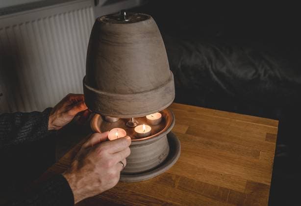 IMAGO Creative: Herbst, Gemütliches Zuhause 14 October 2022: young warmly dressed man warms his hands in a cold apartment without light on a tealight heater to save electricity and gas. homemade tealight stove, DIY heater made of plant pot and tealight candles *** junger warm angezogener Mann wärmt sich die Hände in einer kalten Wohnung ohne Licht an einer Teelichtheizung um Strom und Gas zu sparen. selbstgebauter Teelicht Ofen, DIY Heizung aus Pflanzentopf und Teelicht Kerzen