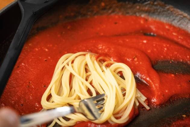 10 July 2022: Spaghetti noodles mixed in a pan with tomato sauce. Cooking spaghetti napoli *** Spaghetti Nudeln in einer Pfanne mit Tomaten Soße gemischt. Spaghetti Napoli kochen