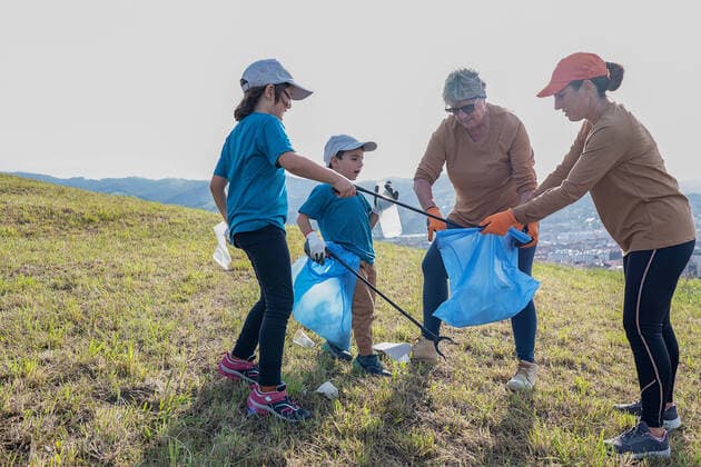 Cleanup volunteers picking up trash in garbage bags with sticks on grassy ground during environmental campaign in countryside, Model released HodeiUnzueta_ID966_36344_052 Copyright: xHodeixUnzuetax MR