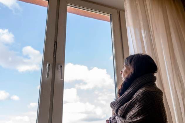 Thoughtful woman wrapped in blanket looking through window at home model released, Symbolfoto property released, ANAF00176
