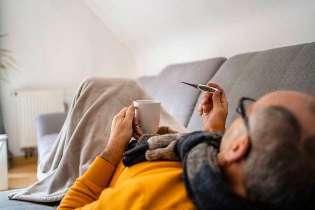 Man measuring fever through thermometer lying on sofa at home model released, Symbolfoto property released, DIGF19024