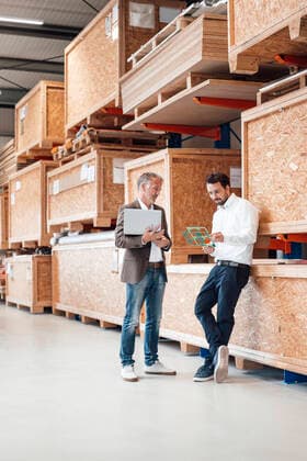 IMAGO Creative: Business, Inflation und Lieferketten Businessman holding laptop talking to colleague standing in warehouse model released, Symbolfoto property released, JOSEF13838