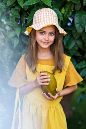 IMAGO Creative: Sommer, Sommertage im Garten Smiling girl wearing hat standing with mango in front of plant model released, Symbolfoto, MEGF00131
