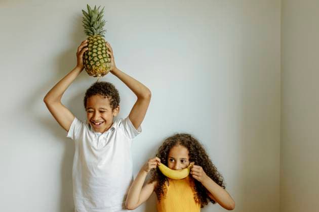 Happy boy holding pineapple above head by sister covering lips with banana in front of wall model released, Symbolfoto property released, VIVF00018