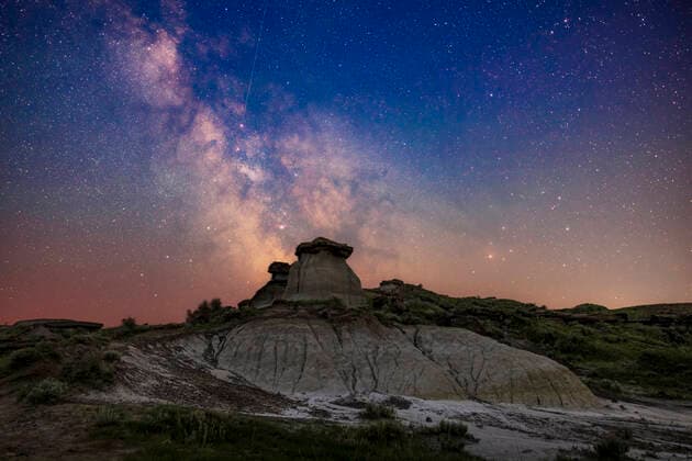 The galactic centre area in Sagittarius (at left) and Scorpius (at right) low in the south on a summer night at Dinosaur Provincial Park, Alberta. This was June 30 July 1, 2022. Being just 10 days after summer solstice and at latitude +50Â° North, the sky even to the south still has a blue tint from all-night twilight. I made no attempt to neutralize the sky colouration. In addition, some haze from smoke discoloured the sky and reduced transparency and contrast low in the sky. Many of the nebulas and star clusters in this part of the Milky Way are visible, many of them showpiece Messier objects for binoculars and telescopes. The colourful area around the star Rho Ophiuchi above Antares is at right, though muted here by the smoke and haze. Copyright: xAlanxDyerx ADY-NOV-22-71