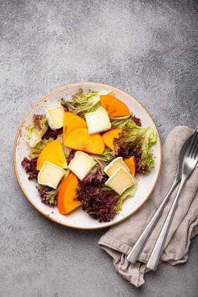 Healthy vegetarian persimmon salad with brie top view Top view flat lay persimmon salad with brie cheese and fresh salad leaves on white plate and stone gray background, seasonal fruit salad as appetizer, vegetarian healthy food Copyright: xZoonar.com OlenaxYeromenkox 17833164