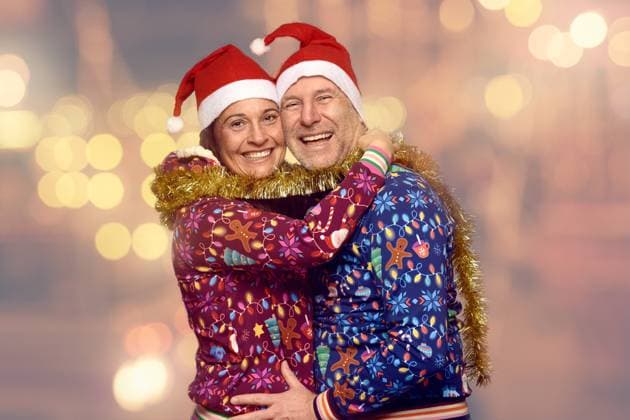 Glückliches Ehepaar in Weihnachtsstimmung Joyful married couple celebrating Christmas together in festive red Santa hats and themed Xmas tops standing hugging and laughing as they turn to smile at the camera against a bokeh of party lights Copyright: xZoonar.com LarsxZahnerx 18908303 ,model released, Symbolfoto ,property released