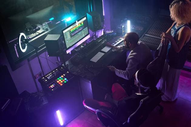 From above of diverse people gathering in modern recording studio with glowing purple neon lights while audio engineer working on computer using editing program, Model released, Property released ManuelRuiz_ID5958_187978_058 Copyright: xManuelxRuizx MR