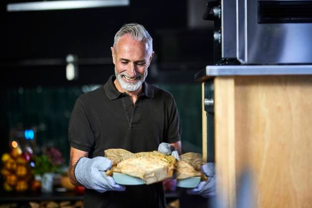 Happy man standing with savory pie by oven in kitchen model released, Symbolfoto property released, FMKF07766