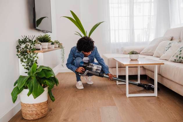 Young woman cleaning under coffee table in living room at home model released, Symbolfoto property released, EBBF06671