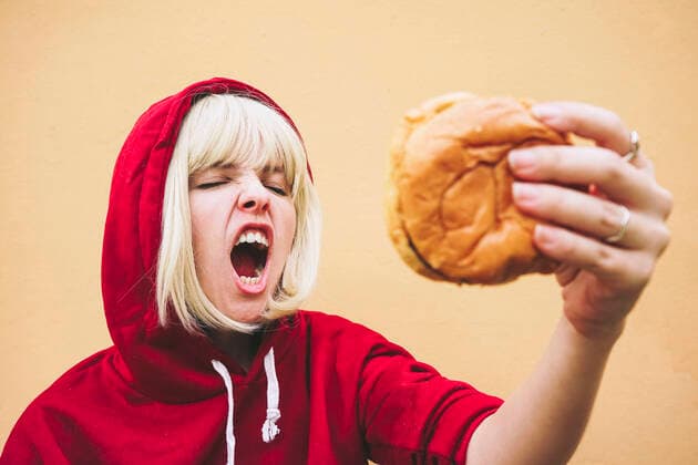 Woman with eyes closed holding hamburger in front of peach wall model released, Symbolfoto, SVCF00212