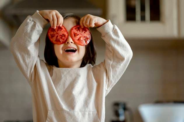 Happy boy holding tomato slices over eyes in kitchen at home model released, Symbolfoto property released, ANAF00294