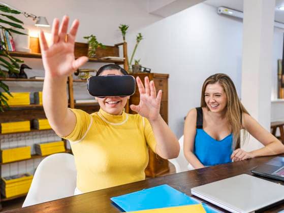 Smiling businesswoman gesturing with VR goggles sitting by friend at table model released, Symbolfoto property released, AMRF00120