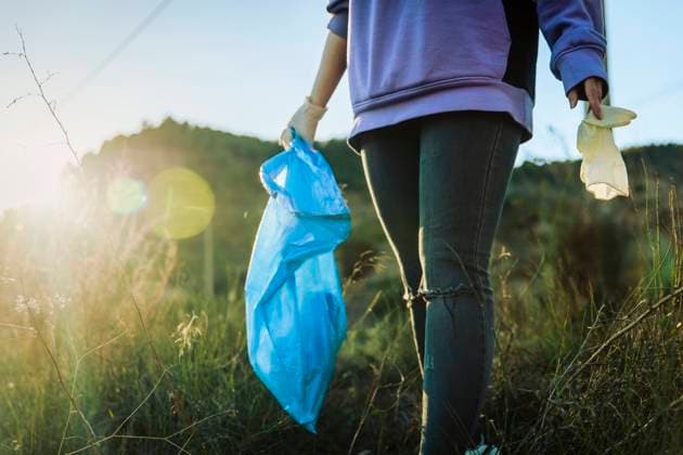 Volunteer walking in grass holding garbage bag on sunset model released, Symbolfoto, ACPF01530
