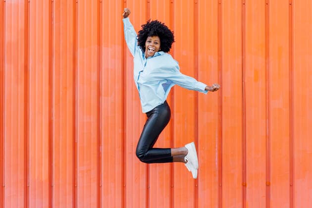 Creative Highlights Symbolbilder Carefree young woman jumping in front of orange wall model released, Symbolfoto, JSMF02479