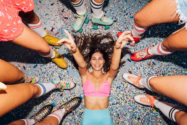 Creative Highlights Symbolbilder Smiling woman gesturing lying on confetti amidst legs of of friends wearing roller skates model released, Symbolfoto, MEUF08556