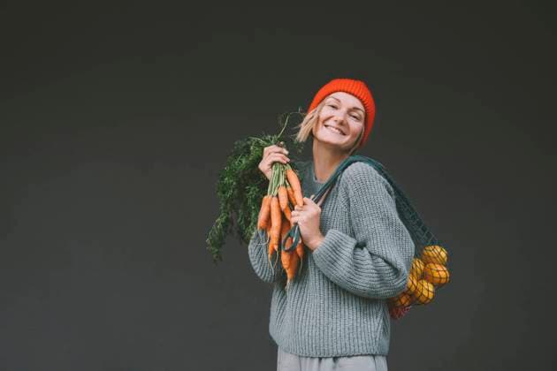 Happy woman holding carrots and mesh bag in front of gray wall model released, Symbolfoto, NDEF00073