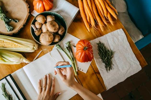 IMAGO Creative, Lifestyle, Tik Tok-Trend thatgirl Directly above view of food stylist writing in diary amidst vegetables on table