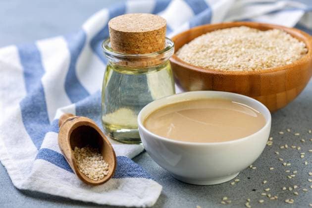 Bottled sesame oil, tahini and white sesame seeds. Cold pressed sesame oil from white sesame, tahini and sesame seeds in wooden bowl on grey textured background, selective focus. Copyright: xZoonar.com MarinaxSaprunovax 13304015