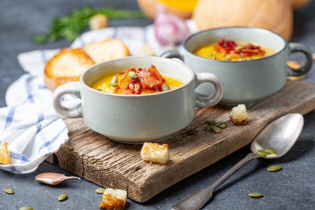 Pumpkin soup with bacon in a rustic style. Pumpkin soup with bacon and croutons in ceramic bowls on an old wooden board and linen cloth on a dark textured background, selective focus. Copyright: xZoonar.com MarinaxSaprunovax 14665656