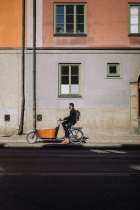 Businessman riding cargo bike against building on sunny day