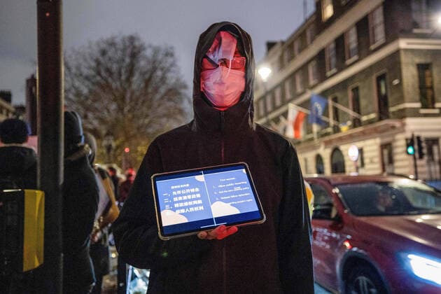 December 5, 2022, London, United Kingdom: A protester having multiple face masks on his face and holding a tablet illustrating the demands from the Chinese to their government during the demonstration outside the Chinese Embassy in London. Chinese students who are currently studying in London gathered at the Chinese Embassy in London to protest against the lockdown policy in China. A massive wave of protests outbroke in China last week since 10 people were killed in a Urumqi in the Northwest region of China due to the inhumane COVID lockdown policy. London United Kingdom - ZUMAs197 20221205_zaa_s197_035 Copyright: xHestherxNgx