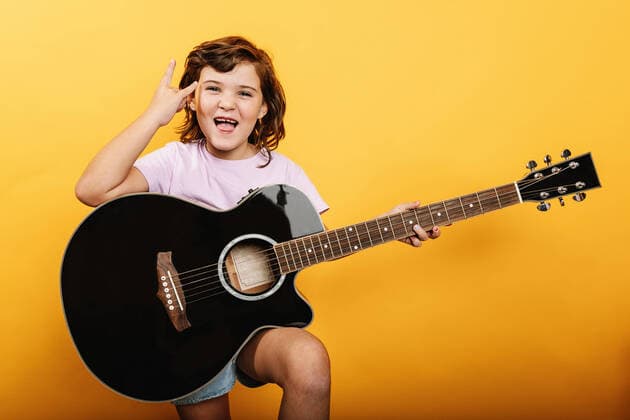 Creative Highlights Symbolbilder Happy kid in pink t shirt with mouth opened showing horn gesture while playing acoustic guitar against yellow background, Model released HodeiUnzueta_ID7769_234933_024 Copyright: xHodeixUnzuetax MR