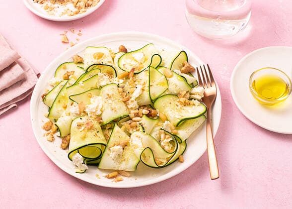 From above fresh salad of thin sliced ripe zucchini, feta cheese and pine nuts in white plate on table pink background OlgaVila_ID10586_320788_003 Copyright: xOlgaxVilax Model Released
