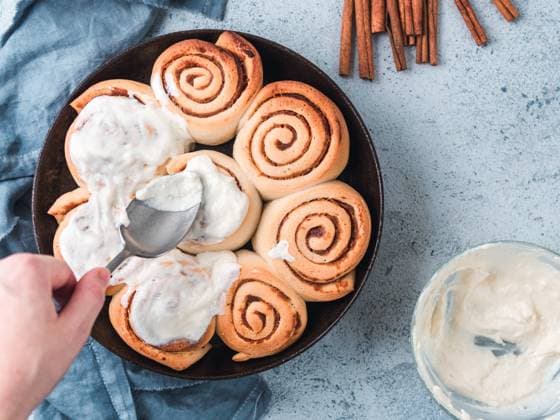 Hand Spreading Frosting on Cinnamon Rolls, copy space Woman s Hand Spreading Frosting on Cinnamon Rolls in Skillet. Vegan swedish cinnamon buns Kanelbullar with pumpkin spice,topping vegan cream cheese. Top view or flat lay. Copy space for text Copyright: xZoonar.com OlgaxSergeevax 15963677