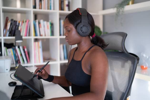 Young African American woman listening to music and drawing on graphic table with stylus while sitting at desk and working on remote freelance project at home OscarDeDios_ID10628_321772_002 Copyright: xOscarxDexDiosx Model Released