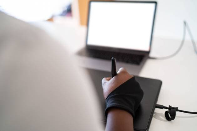 Back view anonymous African American woman using laptop with blank screen and graphic tablet to create illustration during work on creative project in home office OscarDeDios_ID10628_321785_012 Copyright: xOscarxDexDiosx Model Released